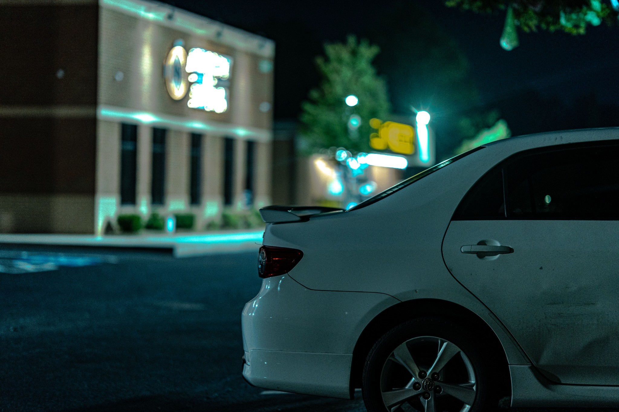 White car beneath nighttime storefront lights — photography by Andrew Frady